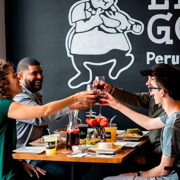 Four people toasting drinks at a table filled with Peruvian food and drinks at El Gordo.