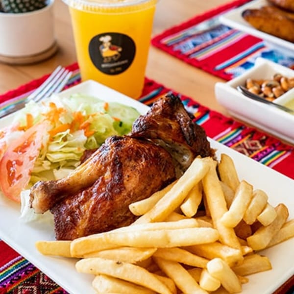 Peruvian roasted chicken with golden fries, fresh salad, and a drink on a colorful placemat.