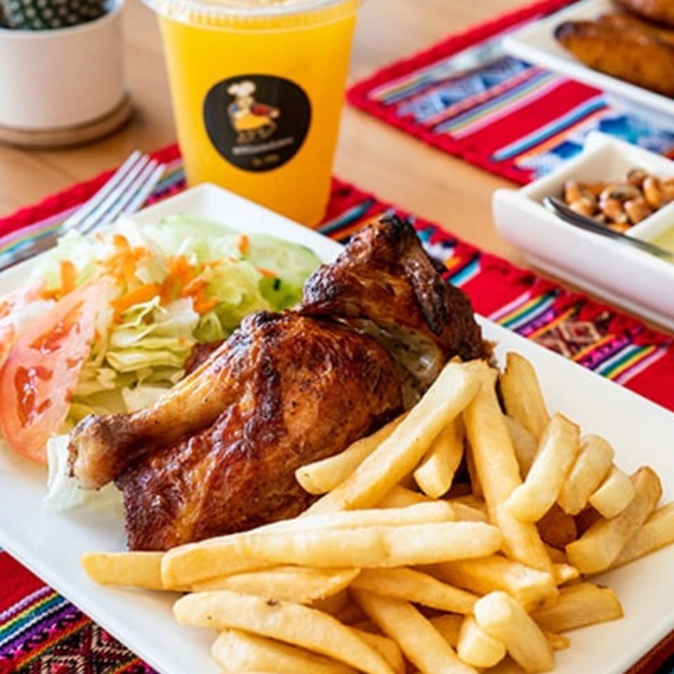 Peruvian roasted chicken with golden fries, fresh salad, and a drink on a colorful placemat.