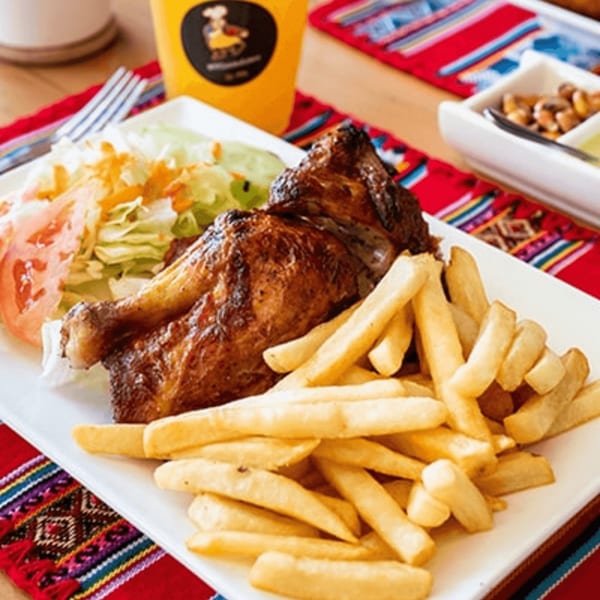Peruvian rotisserie chicken with golden fries and a fresh side salad on a white plate.
