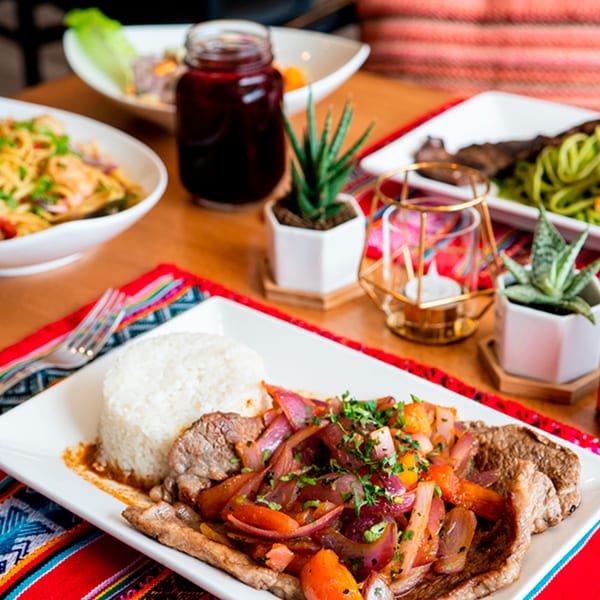 Peruvian Lomo Saltado with rice, a drink, and other dishes on a vibrant tablecloth.