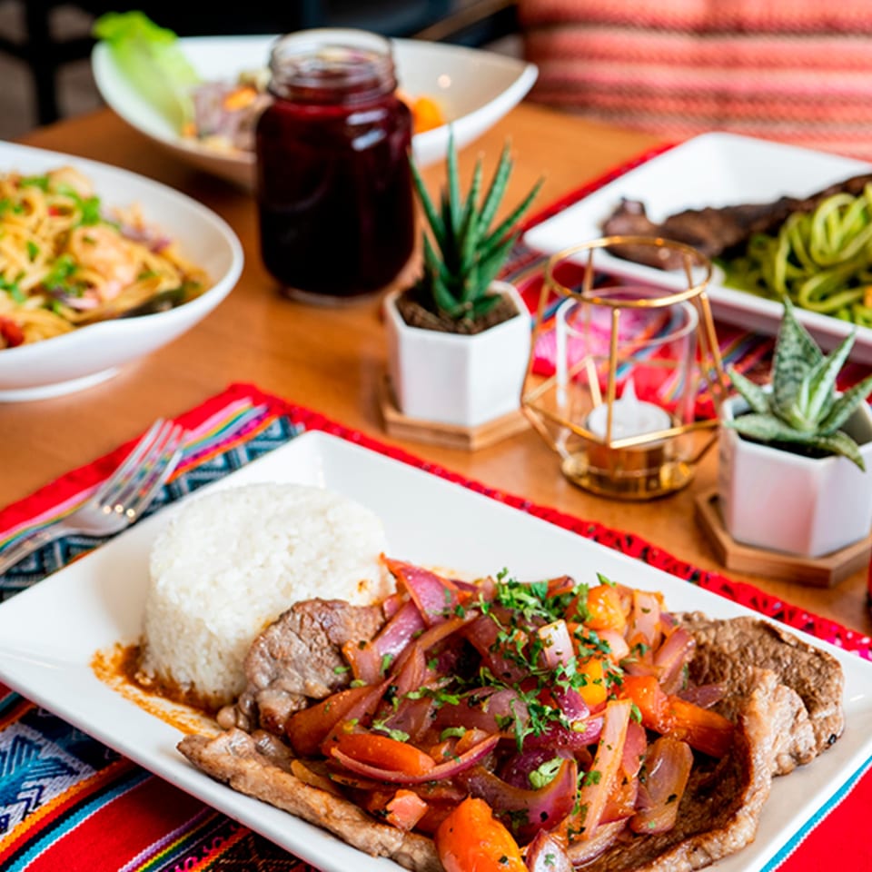 Peruvian Lomo Saltado with rice, a drink, and other dishes on a vibrant tablecloth.
