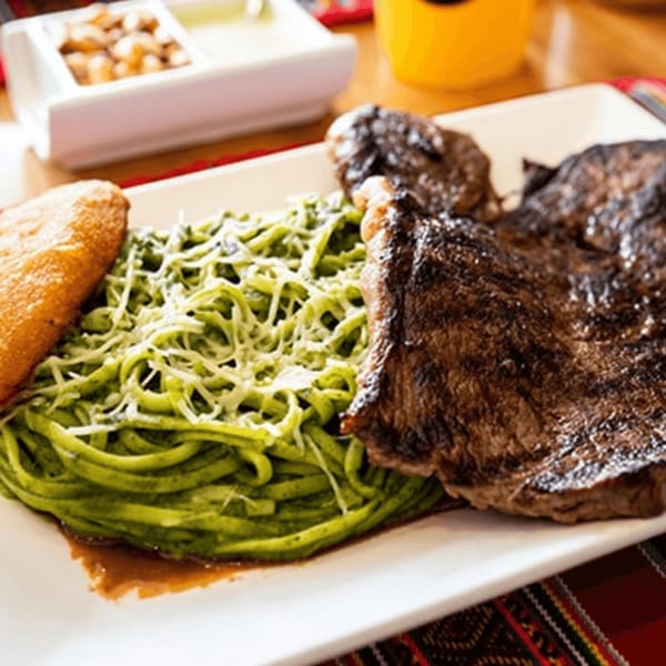 Peruvian steak with green spaghetti and a golden fried plantain on a white plate.
