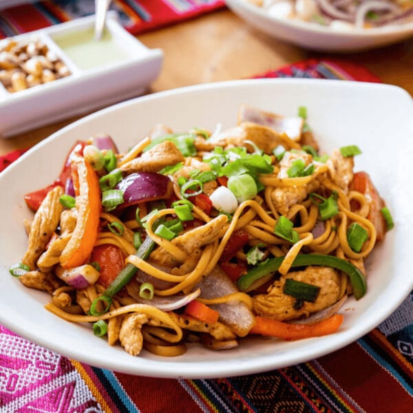 Peruvian Lomo Saltado with chicken, noodles, red onions, and bell peppers, garnished with green onions.