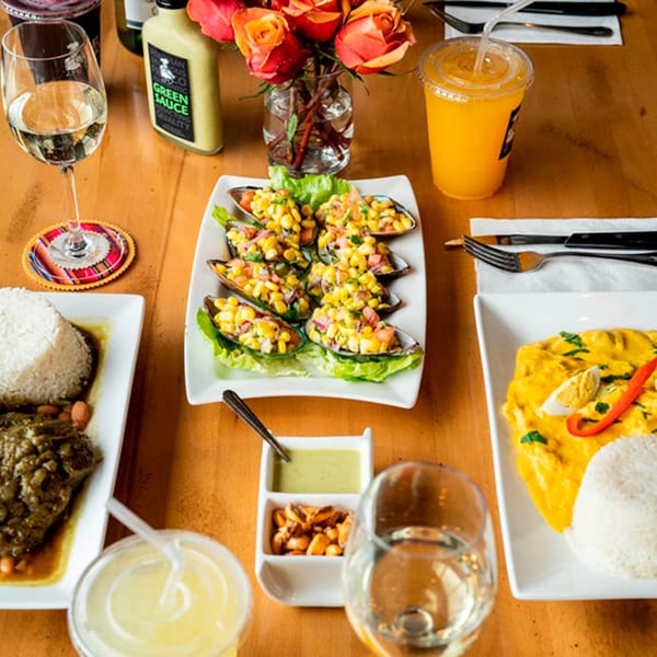 A table laden with Peruvian dishes, including mussels with corn, a yellow stew, and rice.
