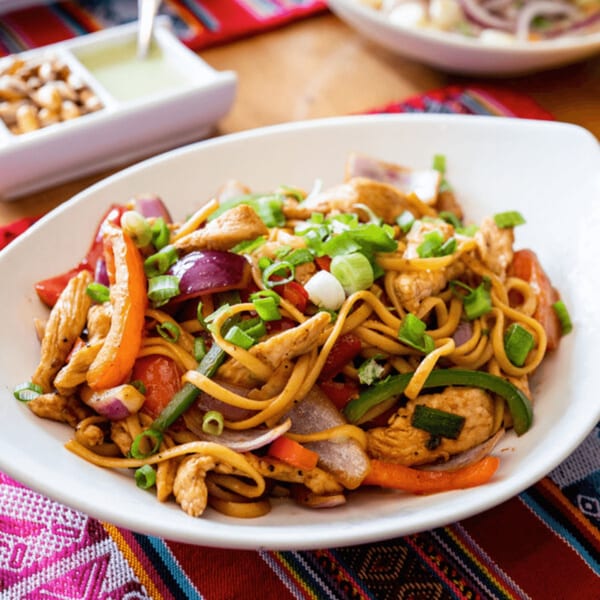 Peruvian Lomo Saltado with chicken, noodles, red onions, and bell peppers, garnished with green onions.