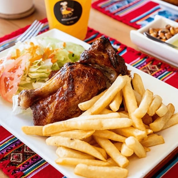Peruvian rotisserie chicken with crispy skin, a side of golden french fries, and fresh salad.
