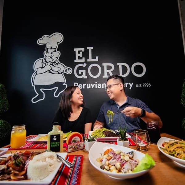 A couple enjoying Peruvian food at El Gordo, with a black wall featuring the restaurant's logo.