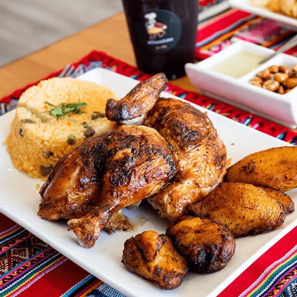Peruvian rotisserie chicken with rice and fried plantains, served on a white plate with a colorful tablecloth.