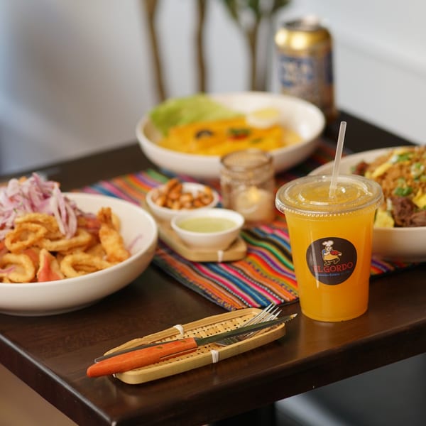 Peruvian dishes, including fried calamari, a yellow stew, and an orange drink, on a colorful placemat.