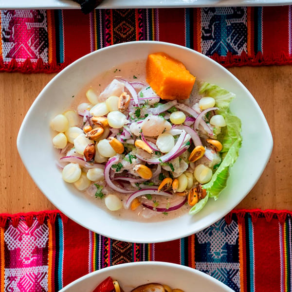 Peruvian ceviche with fish, red onions, corn, toasted corn, sweet potato, and lettuce on a white plate.