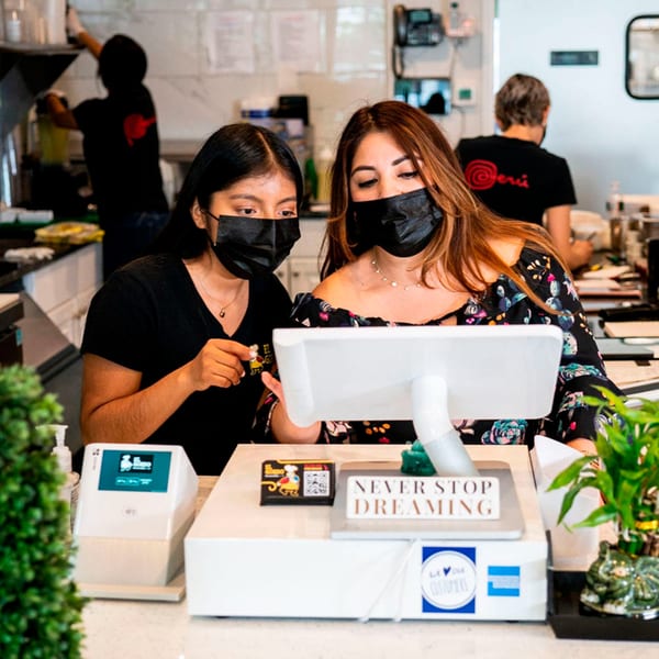 Two masked women at El Gordo Peruvian Eatery looking at a computer screen at the counter.