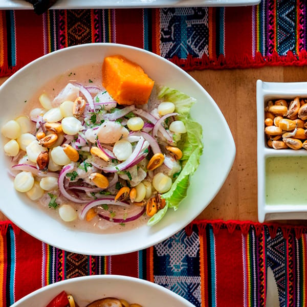 Peruvian ceviche with fish, red onions, corn, and sweet potato, on a colorful woven placemat.