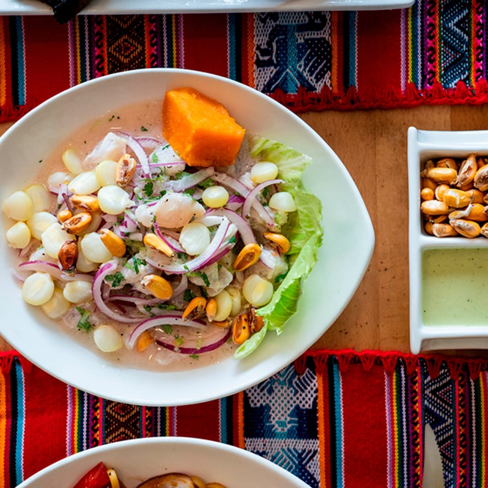 Peruvian ceviche with fish, red onions, corn, and sweet potato, on a colorful woven placemat.