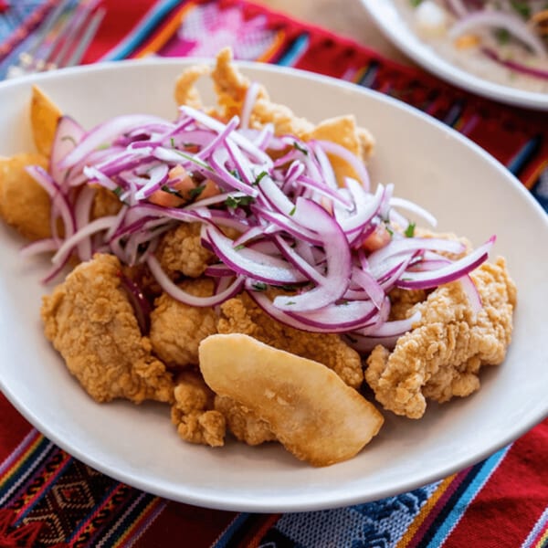 Crispy fried Peruvian chicharrón de pescado with red onion salsa criolla on a white plate.