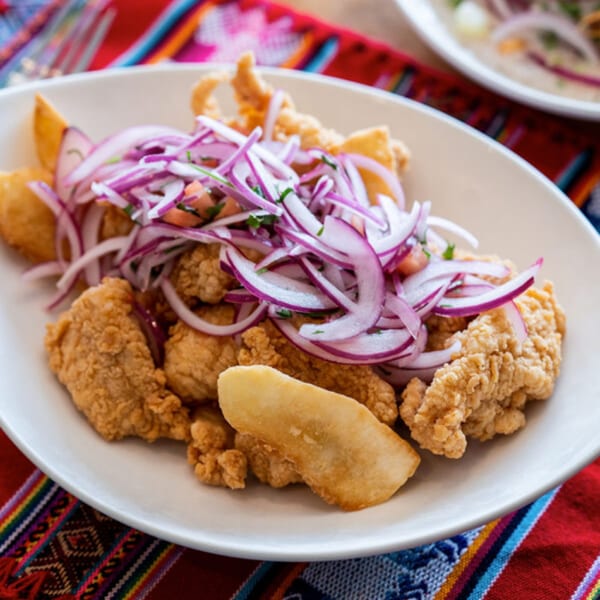 Crispy fried Peruvian chicharrón de pescado with red onion salsa criolla on a white plate.