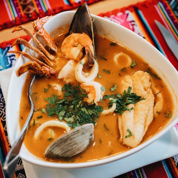 Peruvian seafood soup with crab, shrimp, squid, mussels, and fish in a white bowl.